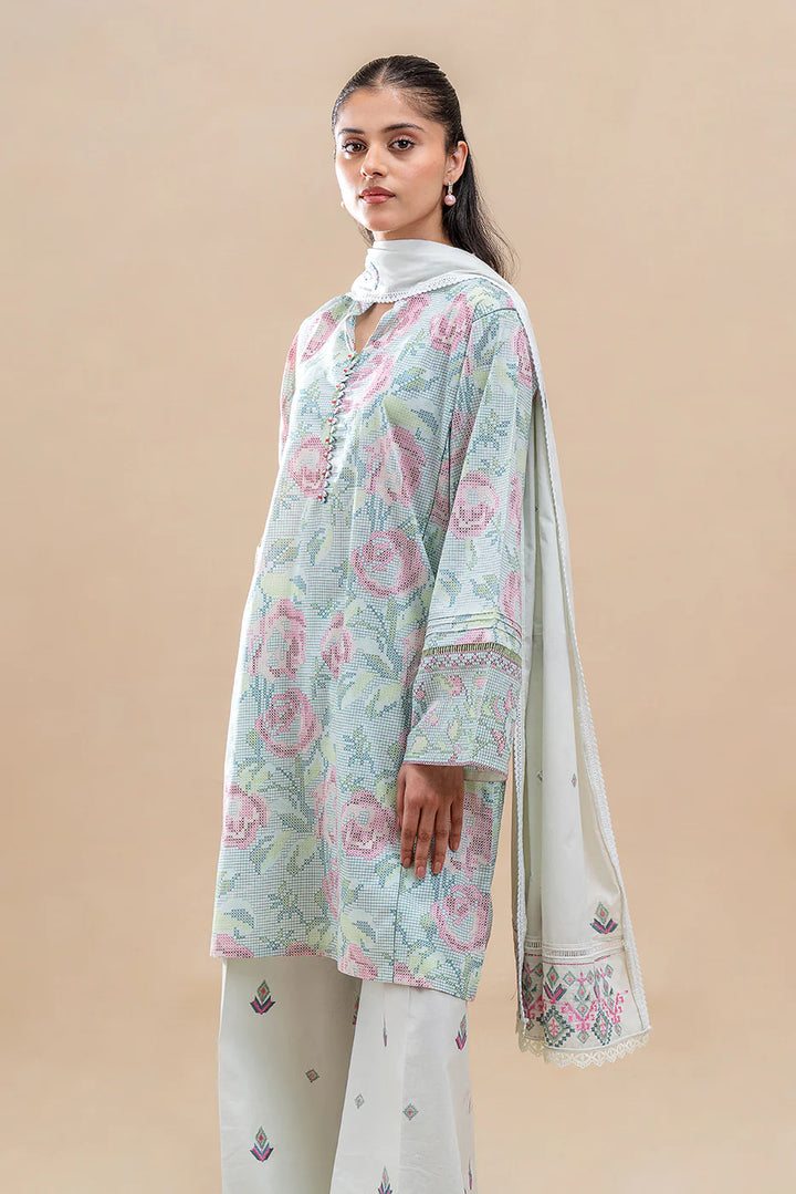 Wearing Pastel Blush, the model stands in soft florals and threadwork—tea-toned lawn shirt with cuff embroidery, matching trousers, and a voil dupatta that completes the quiet symmetry.