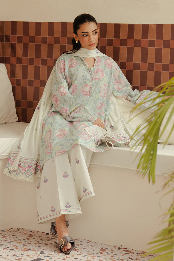 Model sits in Pastel Blush—floral-printed lawn shirt with tonal embroidery, white trousers, and voil dupatta, styled for summer calm.