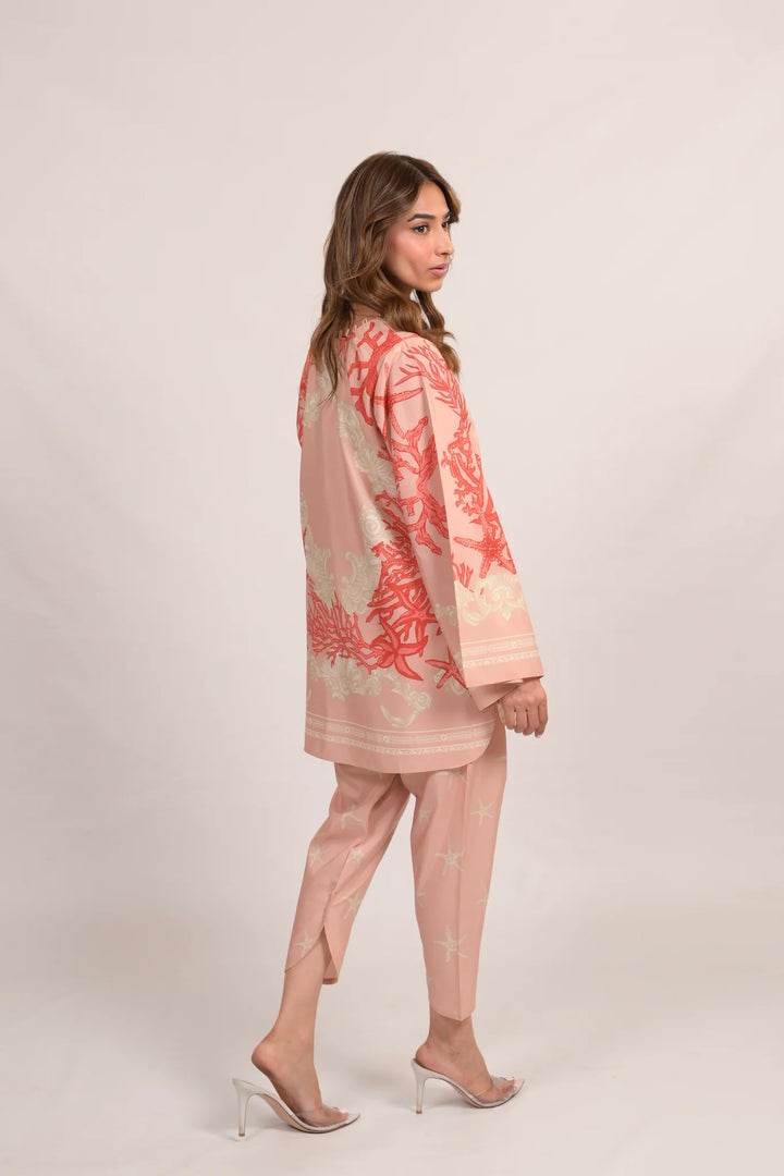 Side profile pose in Marjan A—cotton-silk co-ord in soft pink with coral and starfish motifs, relaxed tunic and matching pants styled with clear heels against a neutral backdrop.