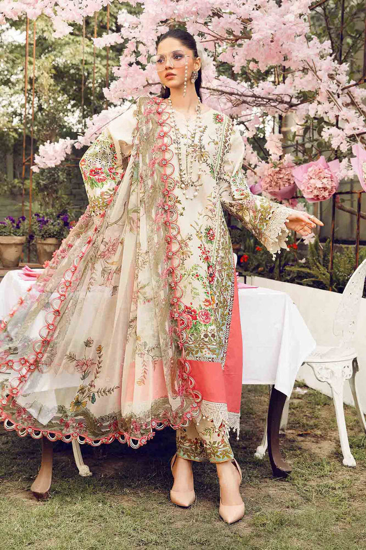 The model stands in a garden setting wearing MPT-2605-A — floral lawn shirt paired with printed trousers and a chiffon dupatta trimmed in pink lace, cherry blossoms framing the scene. Unstitched Mprints ’25 via Nainpreet.
