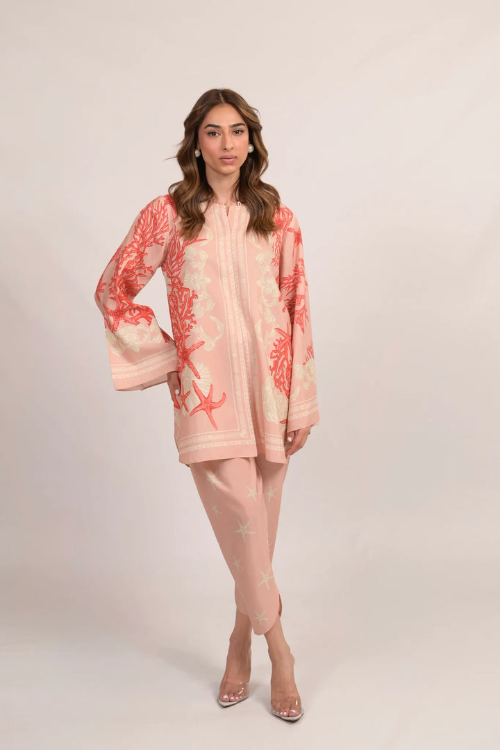 Marjan A co-ord in soft pink—cotton-silk shirt with coral and starfish motifs, paired with matching pants and clear heels against a neutral backdrop.