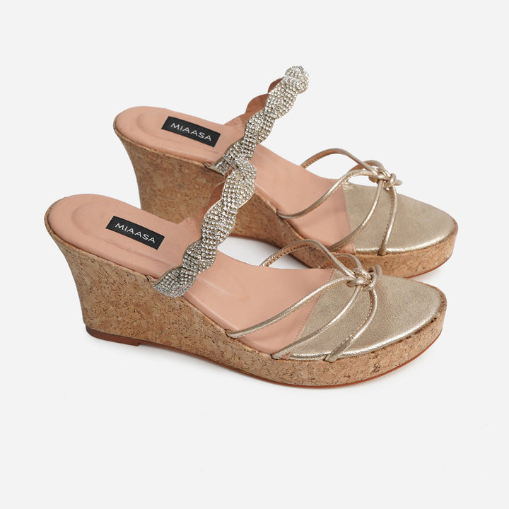 A pair of Anahita Gold wedges from Soleil Eid ’25, featuring cork heels, metallic gold footbeds, and intertwined gold straps. A crystal-studded wave embellishment adds sparkle, blending festive elegance with everyday comfort.