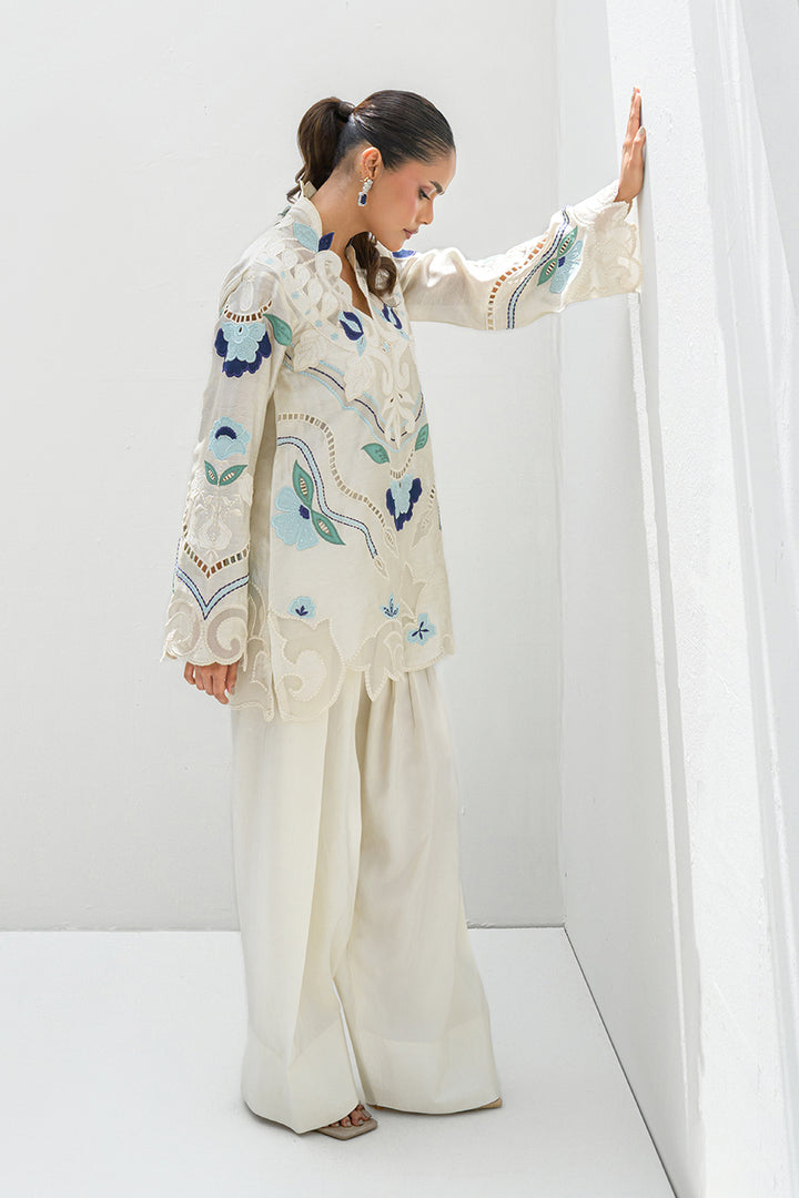 Girl posing against the wall in Azure off-white top with blue and teal embroidery, featuring cutwork details and from Nadia Farooqui’s Deena Eid Edit '25 collection