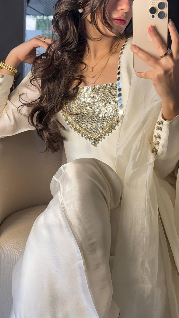 Close-up shot of The Amal Set—white silk kurta with triangular mirror-work neckline, embellished sleeves, and matching dupatta styled in a softly lit room.