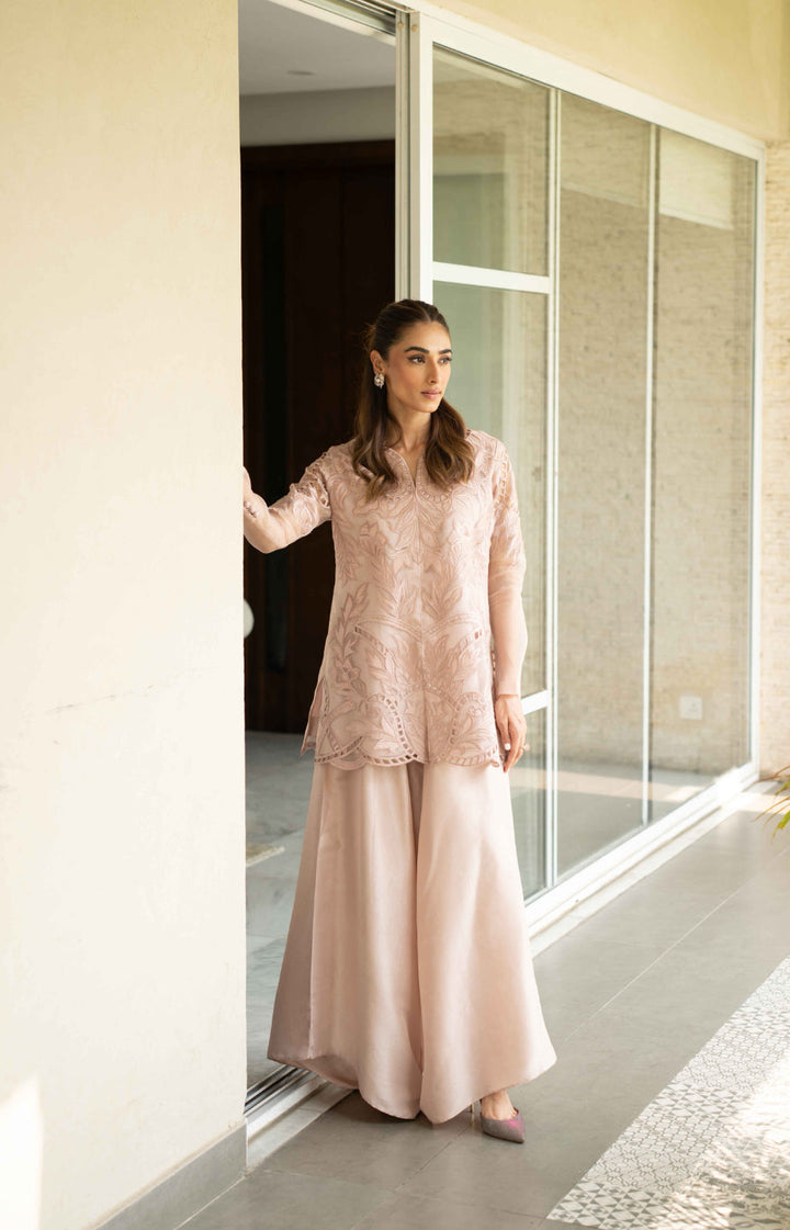 Model stands in Petal Smoke—tea-pink organza jacket with cutwork embroidery and raw silk box trousers, styled for Eid.