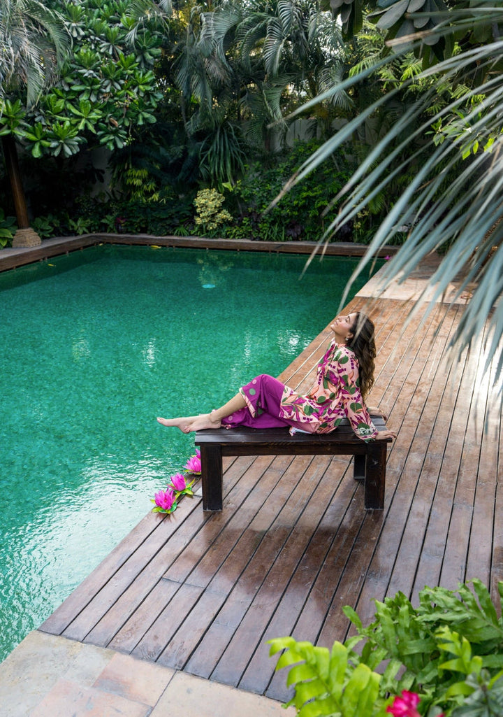 Girl relaxes by pool in Solids Official Amalfi pink-green floral kurti & purple shalwar. A Summer Weekend '25 collection.